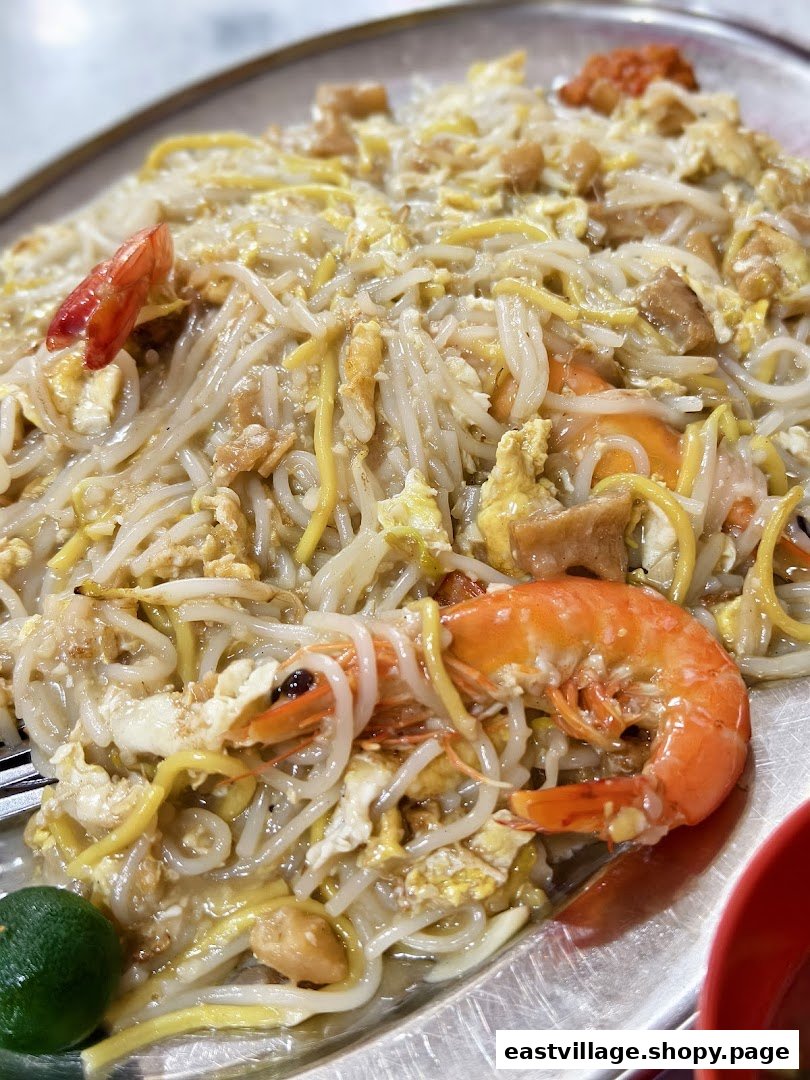 A close-up of a plate of Hokkien Mee with prawns, eggs, and a lime wedge.