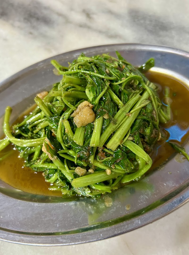 A close-up of stir-fried green vegetables with savory sauce on a metal plate.