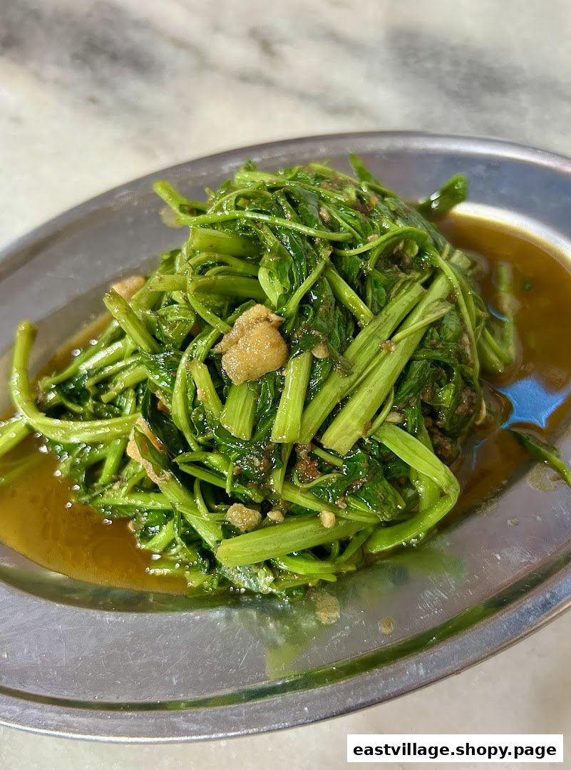 A close-up of stir-fried green vegetables with savory sauce on a metal plate.