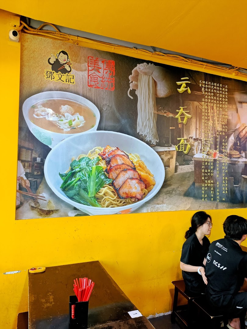 A vibrant interior shot of Deng Wen Ji, featuring a large mural of wonton and char siew noodles, with customers seated at a table.