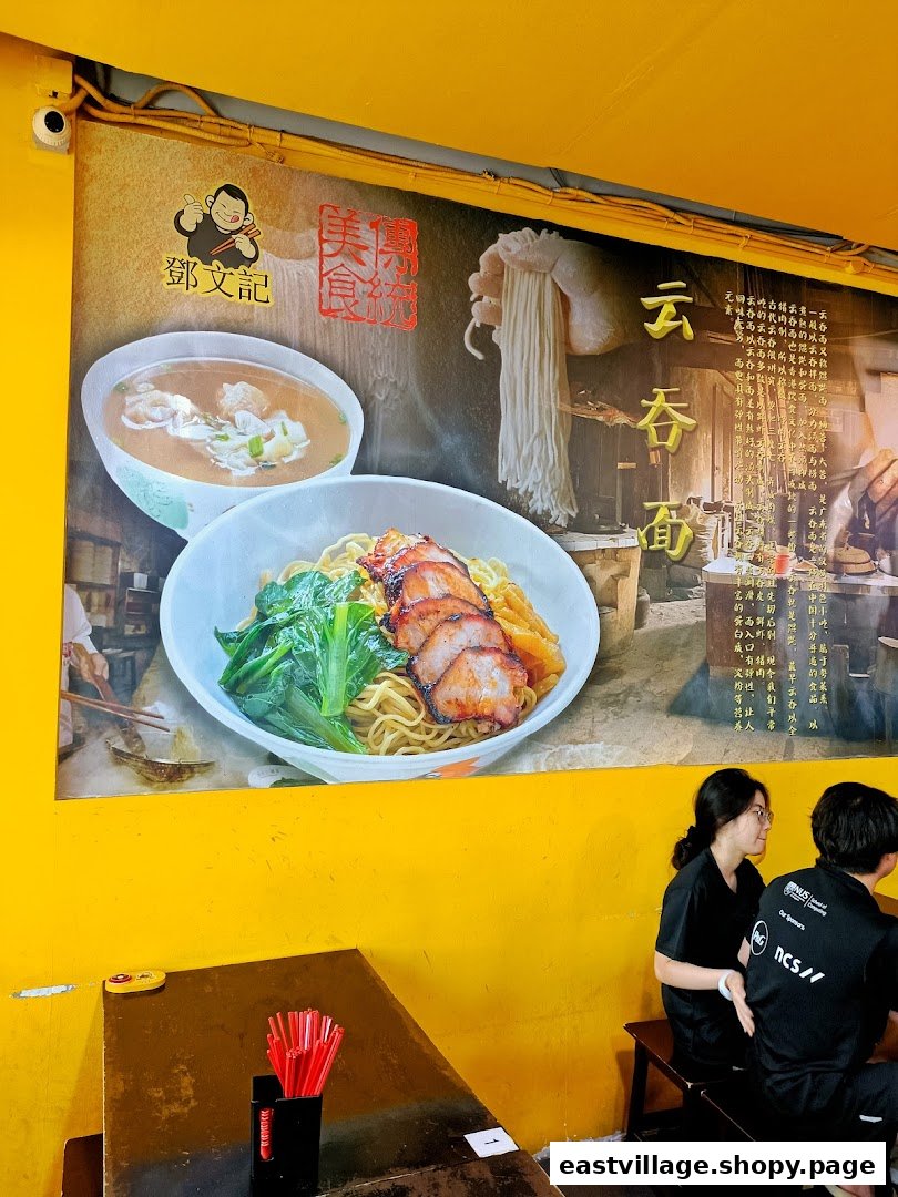 A vibrant interior shot of Deng Wen Ji, featuring a large mural of wonton and char siew noodles, with customers seated at a table.