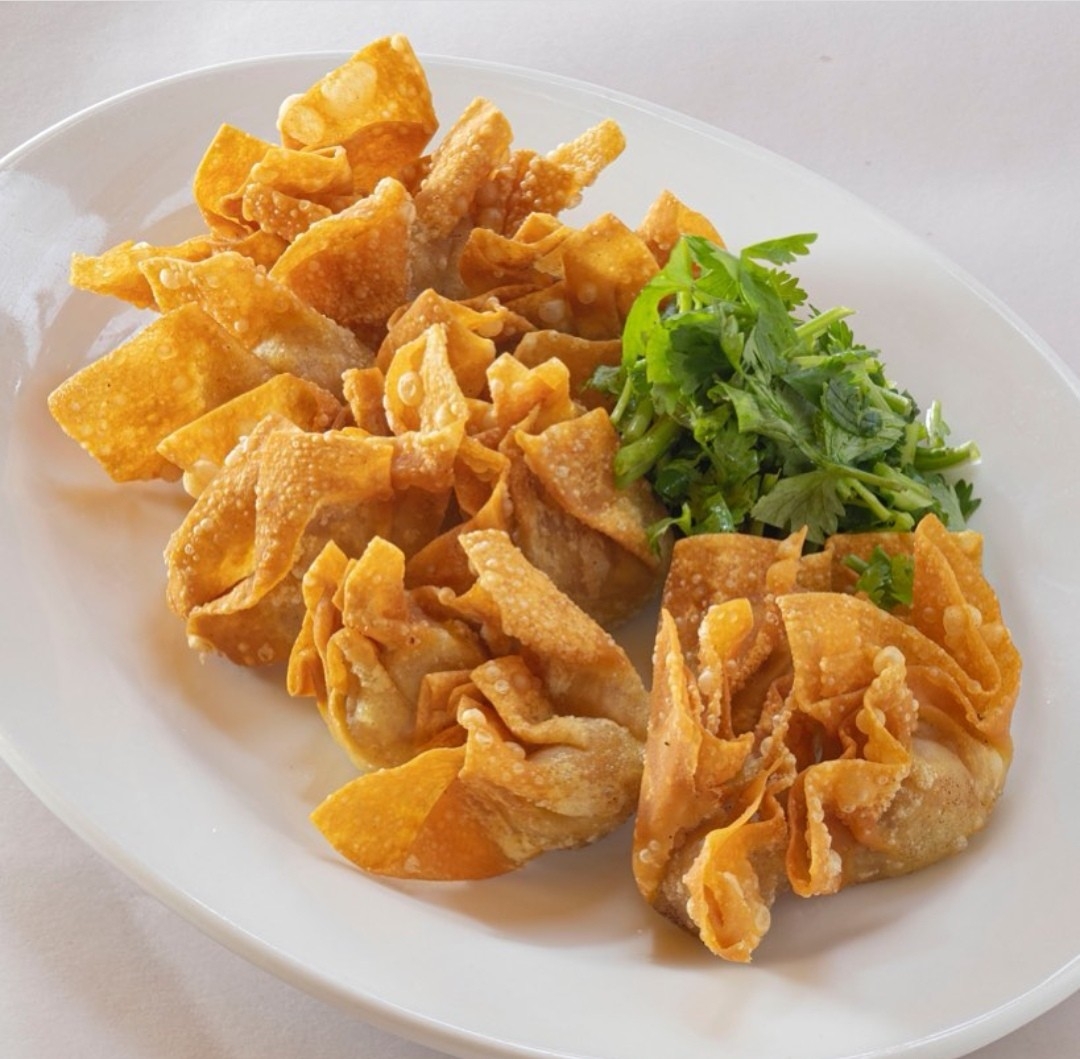 A plate of golden-fried wontons or dumplings served with fresh green herbs.