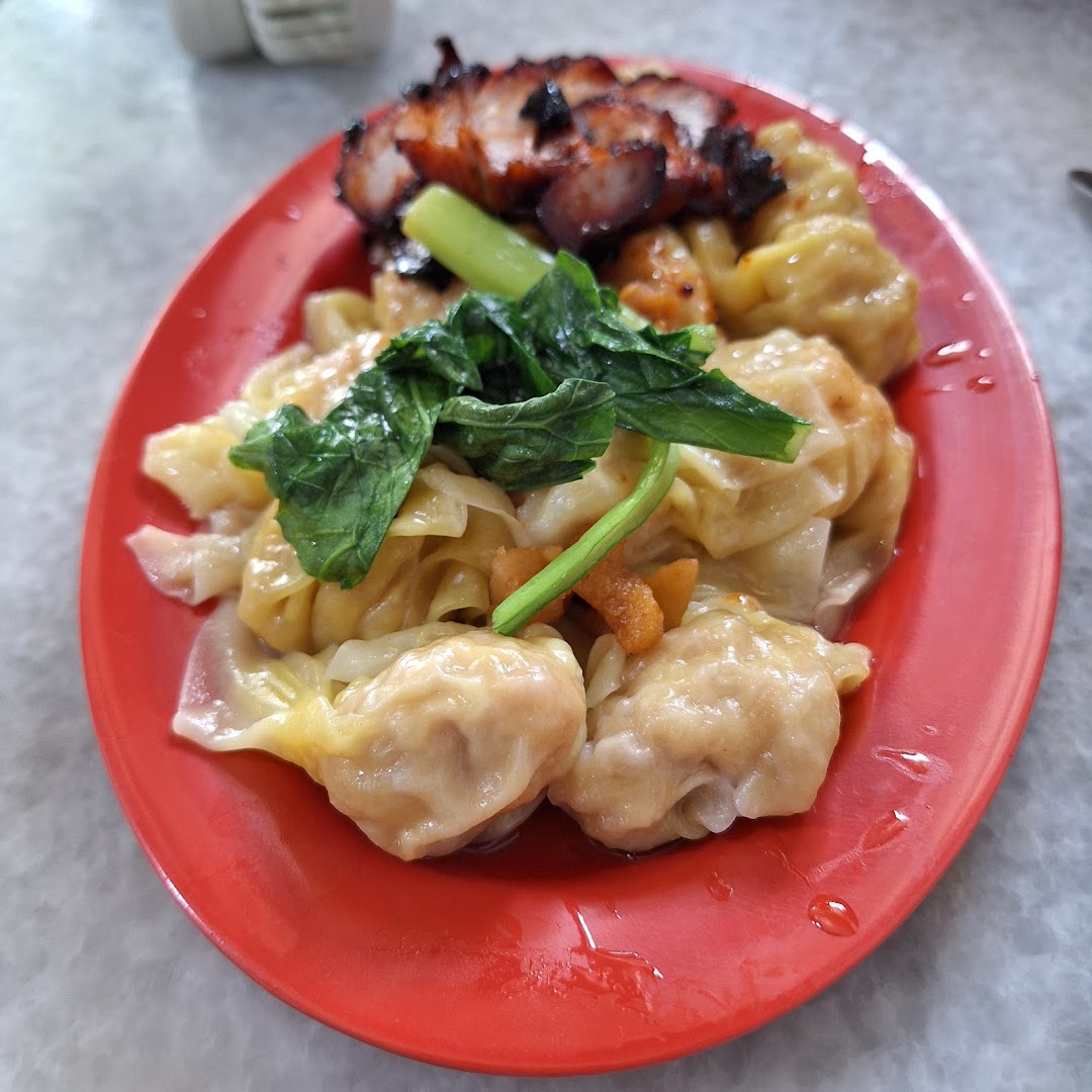 A vibrant red plate holds delicious wontons, char siew, and fresh greens.