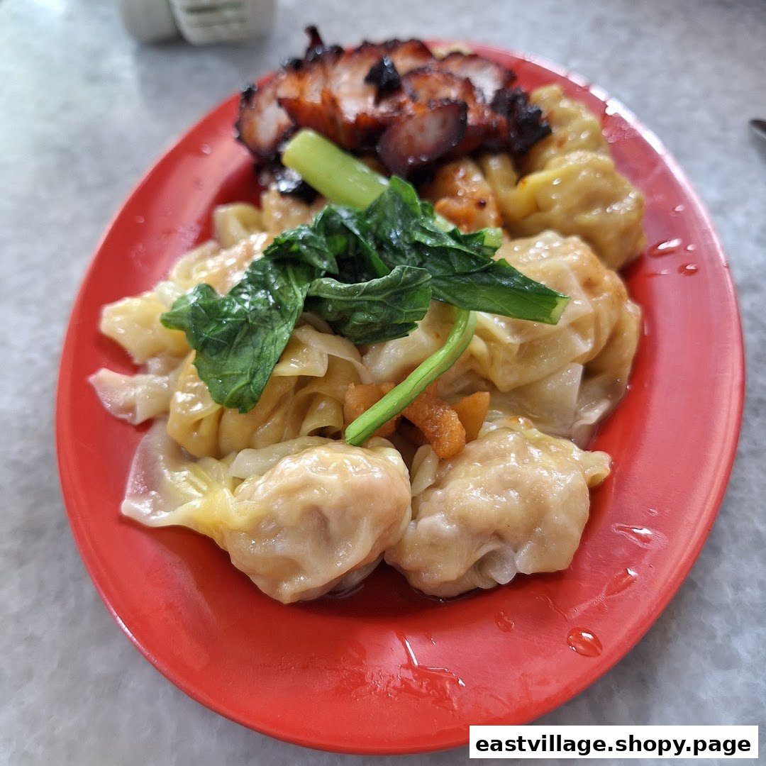 A vibrant red plate holds delicious wontons, char siew, and fresh greens.