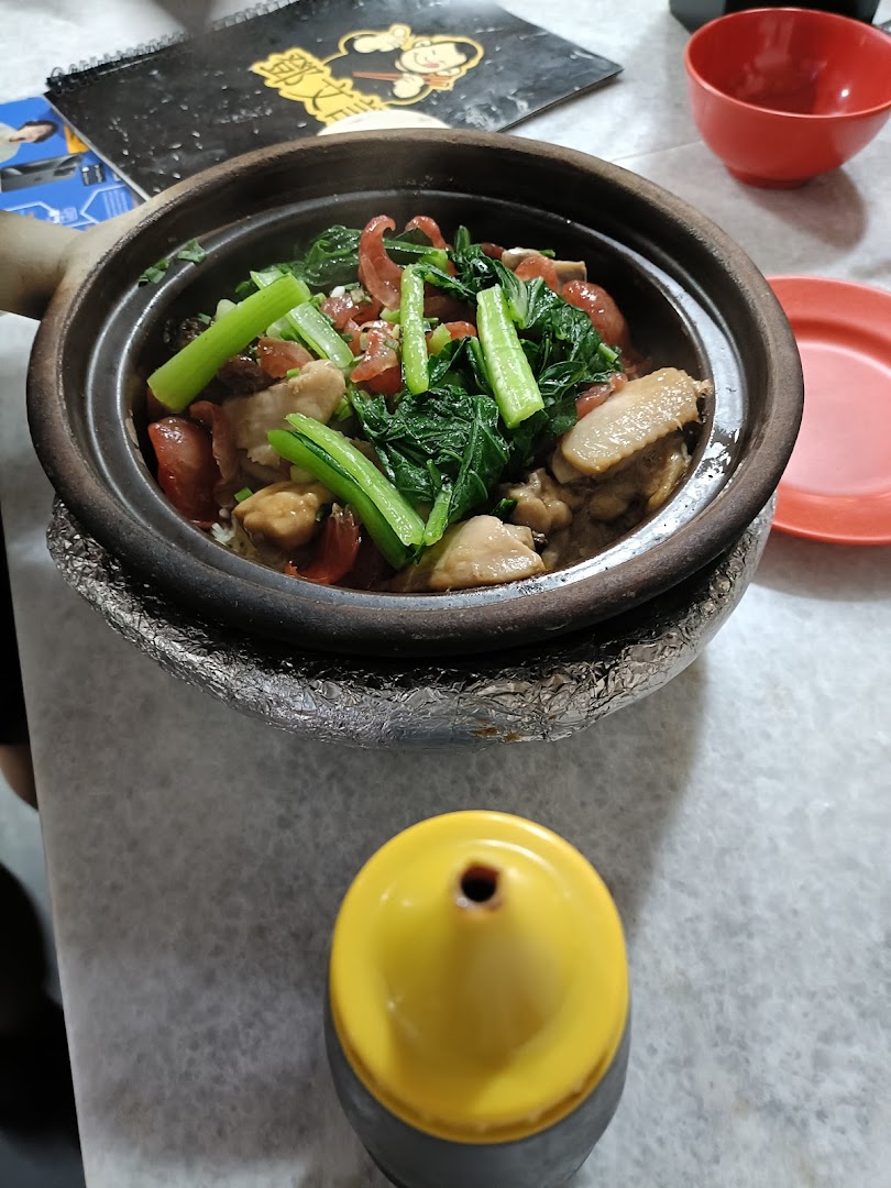 A steaming clay pot dish with chicken, Chinese sausage, and vegetables, served on a table.