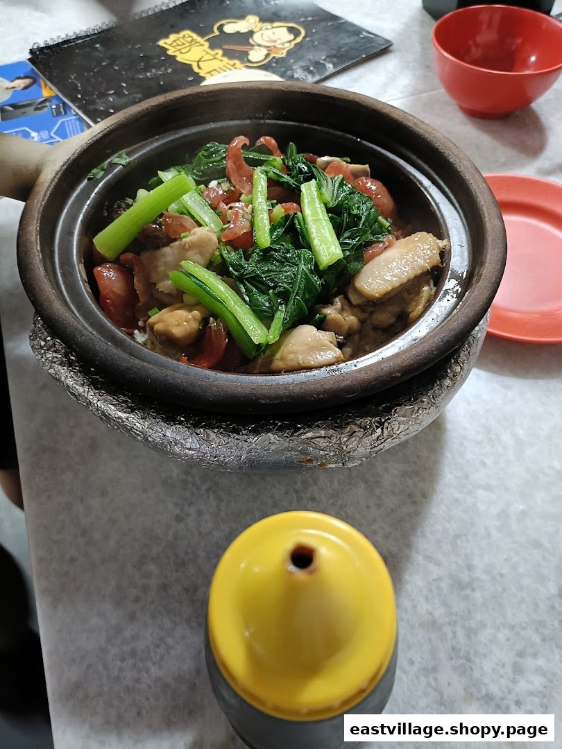 A steaming clay pot dish with chicken, Chinese sausage, and vegetables, served on a table.