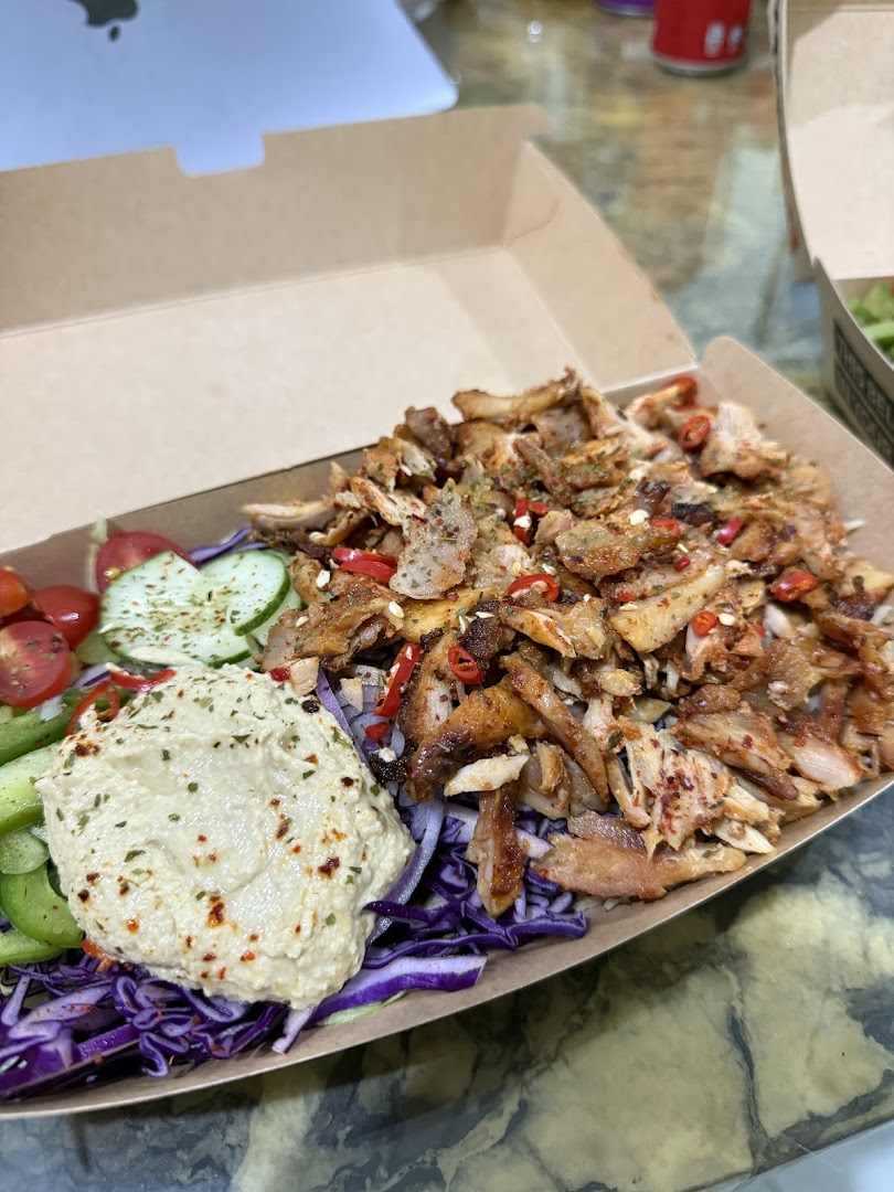 A delicious kebab bowl with seasoned meat, fresh vegetables, and hummus in a takeaway box.