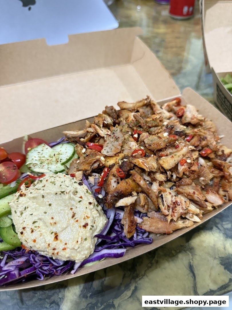 A delicious kebab bowl with seasoned meat, fresh vegetables, and hummus in a takeaway box.