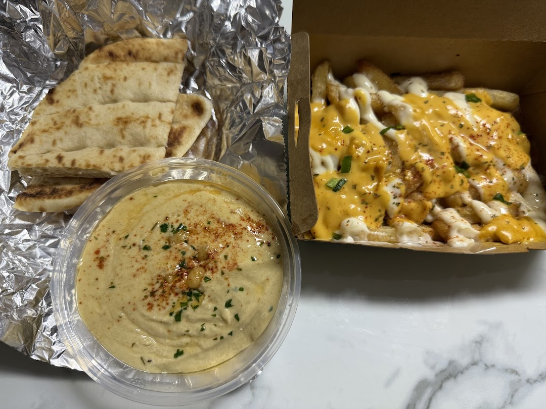 A close-up of creamy hummus with pita bread and a box of loaded fries.