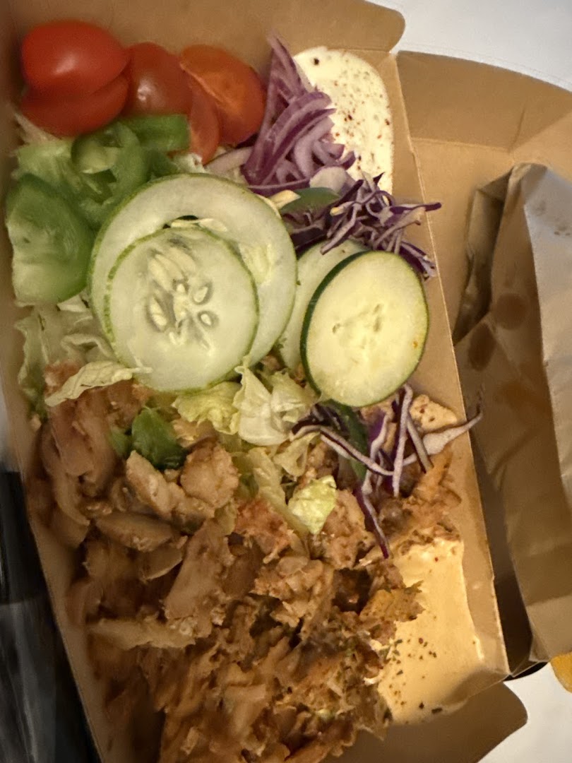 A close-up of a delicious kebab box filled with seasoned meat, fresh vegetables, and sauce.