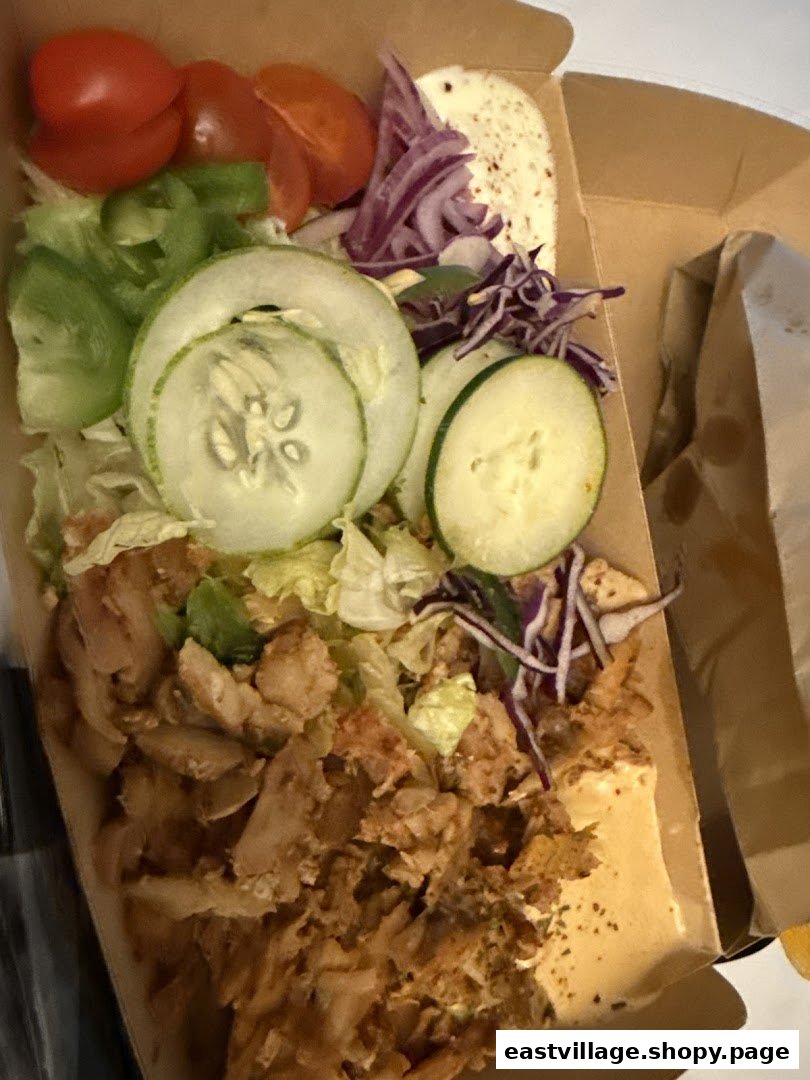 A close-up of a delicious kebab box filled with seasoned meat, fresh vegetables, and sauce.