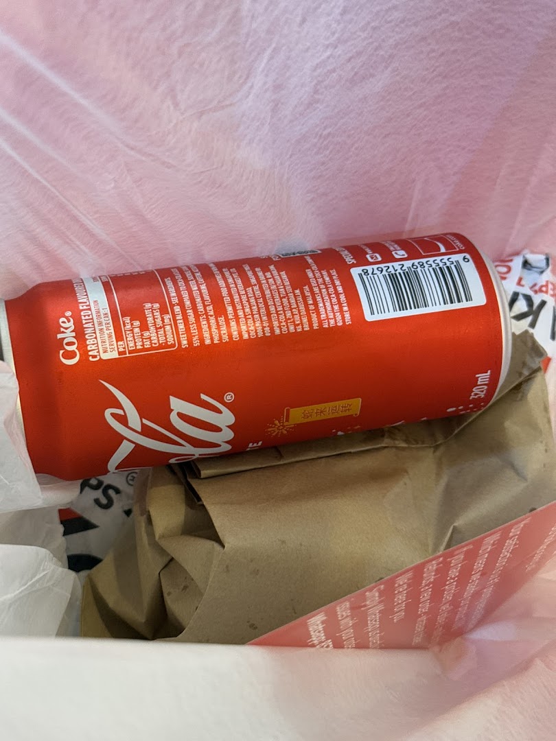A close-up of a Coca-Cola can and a brown paper bag inside a white plastic bag, likely a takeaway order.