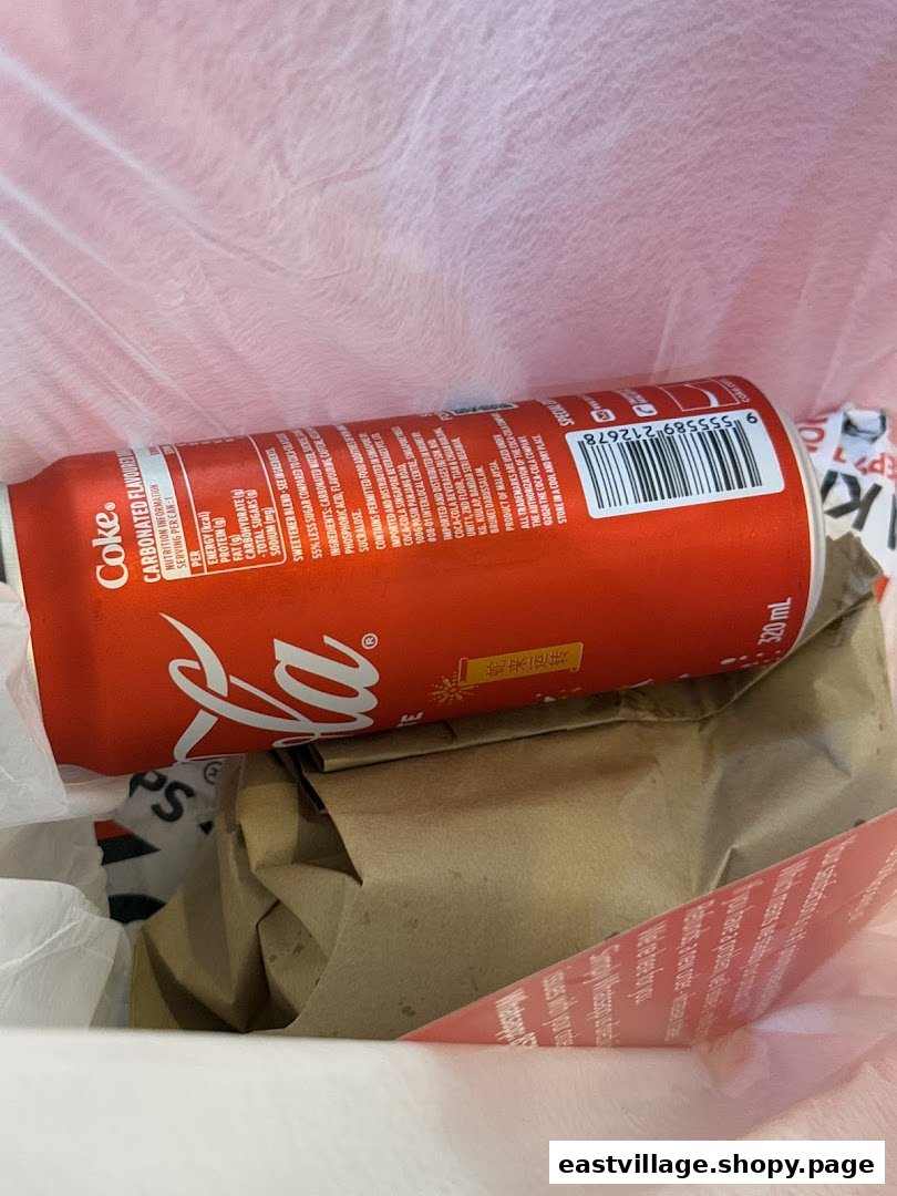 A close-up of a Coca-Cola can and a brown paper bag inside a white plastic bag, likely a takeaway order.