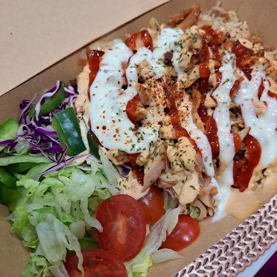 A close-up of a delicious kebab plate featuring meat, rice, fresh salad, and creamy sauces.