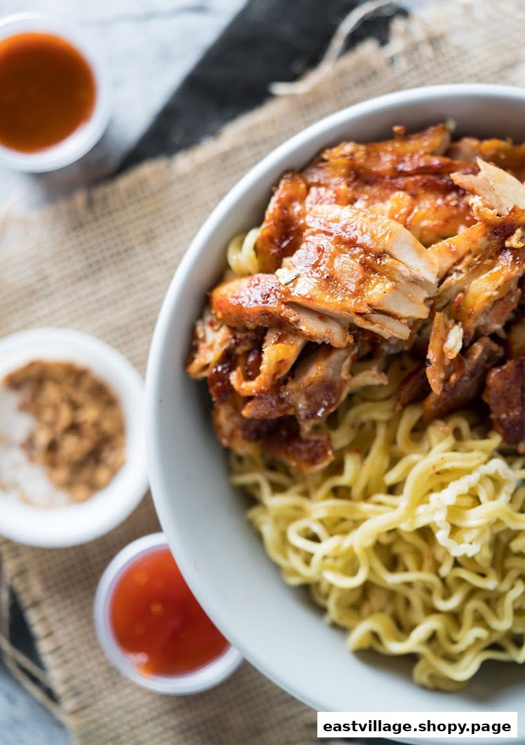 A close-up of a bowl of noodles topped with grilled chicken and side sauces.