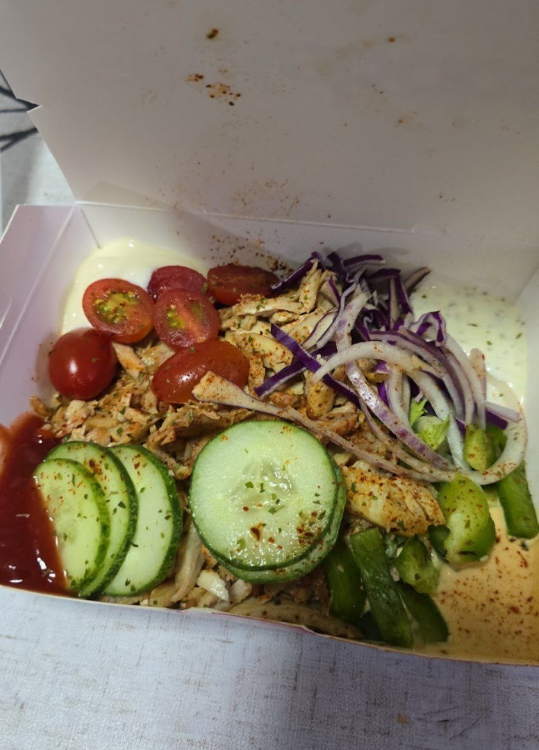 A vibrant kebab bowl with chicken, fresh vegetables, and sauces in a takeaway box.