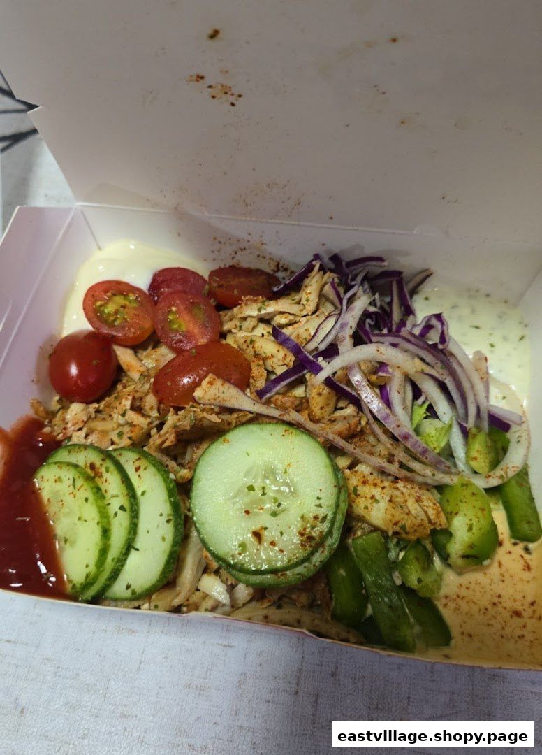 A vibrant kebab bowl with chicken, fresh vegetables, and sauces in a takeaway box.
