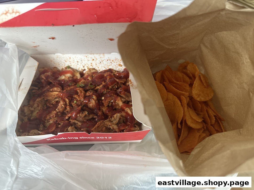 A close-up of a delicious kebab box with meat and sauce, alongside a bag of crispy chips.