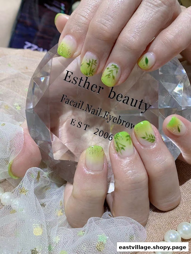 Close-up of hands showcasing a fresh green gradient nail design with delicate leaf art.
