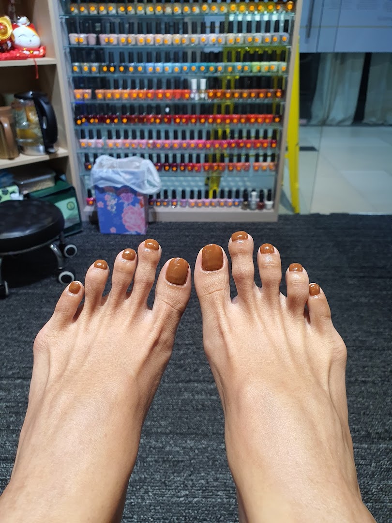 A close-up of feet with freshly painted brown toenails, with a large display of colorful nail polishes in the background.
