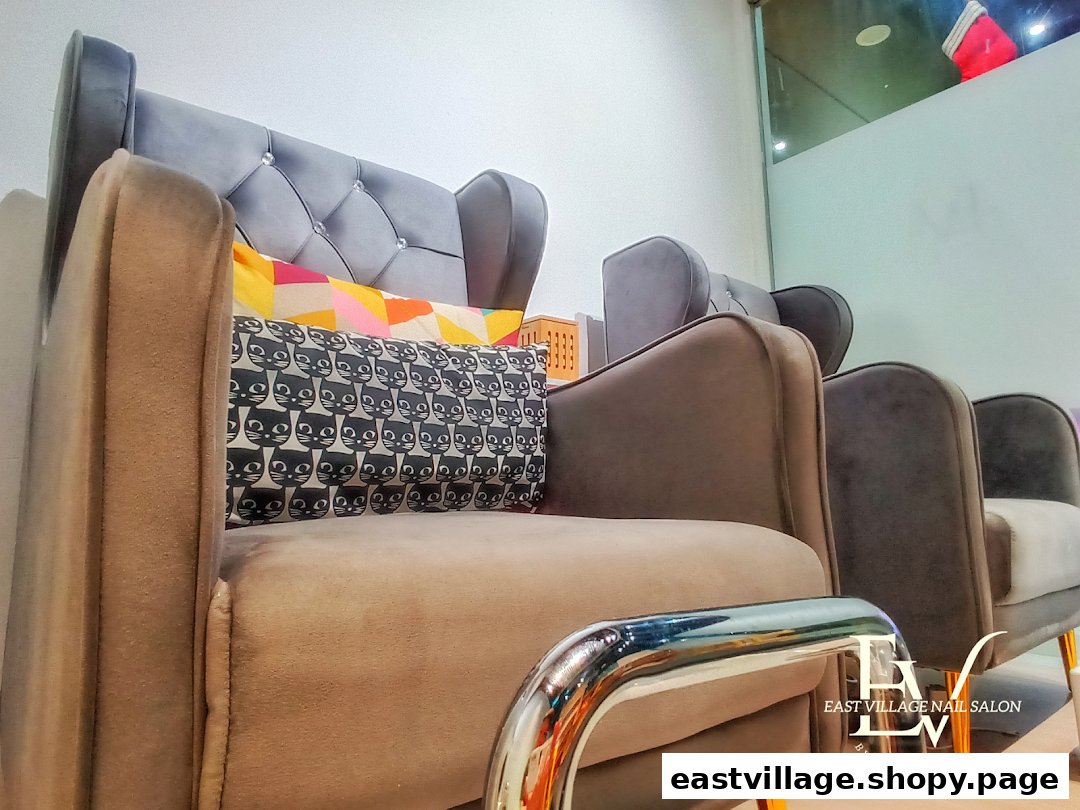 A row of comfortable, plush chairs with decorative pillows inside EV Nail Salon's waiting area.