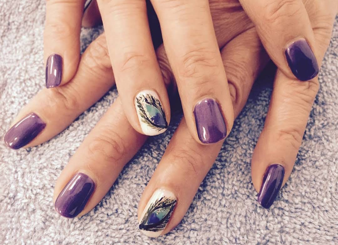 Close-up of hands showcasing purple nail polish with intricate feather design nail art.