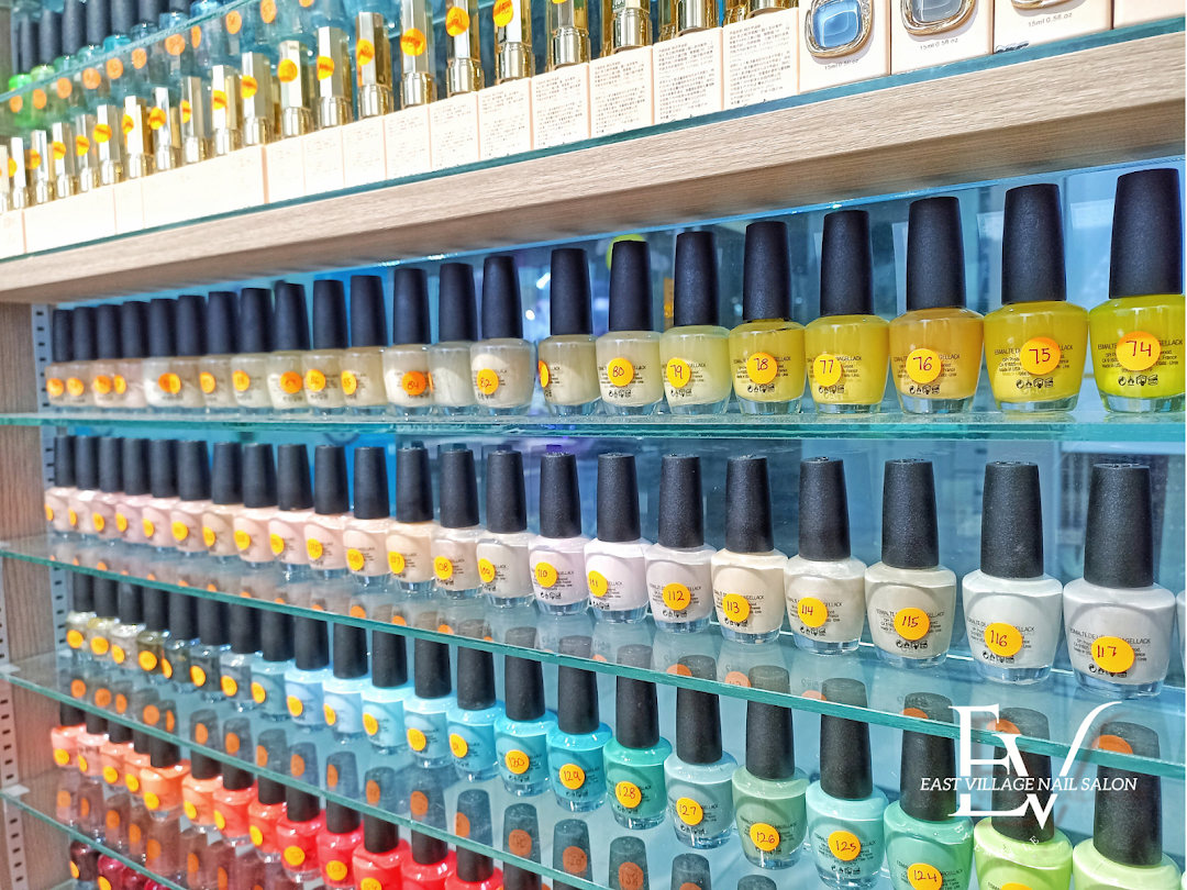A vibrant display of numerous nail polish bottles arranged by color on glass shelves inside EV Nail Salon.
