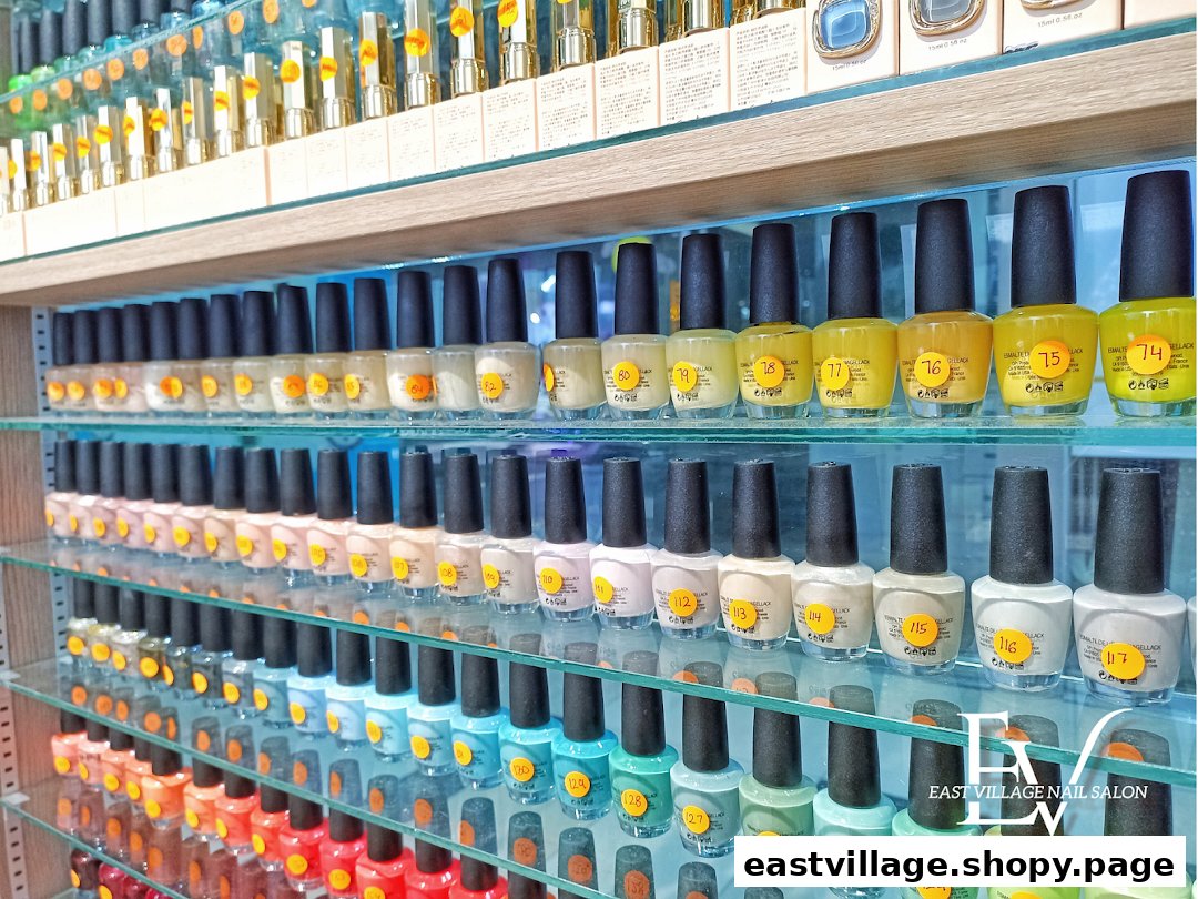 A vibrant display of numerous nail polish bottles arranged by color on glass shelves inside EV Nail Salon.
