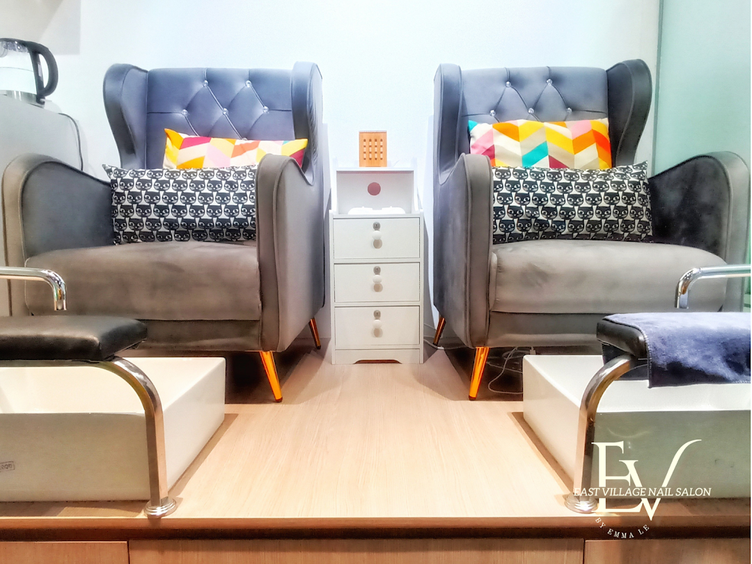 Two plush grey armchairs with colorful pillows and foot baths, set up for a relaxing nail salon experience.