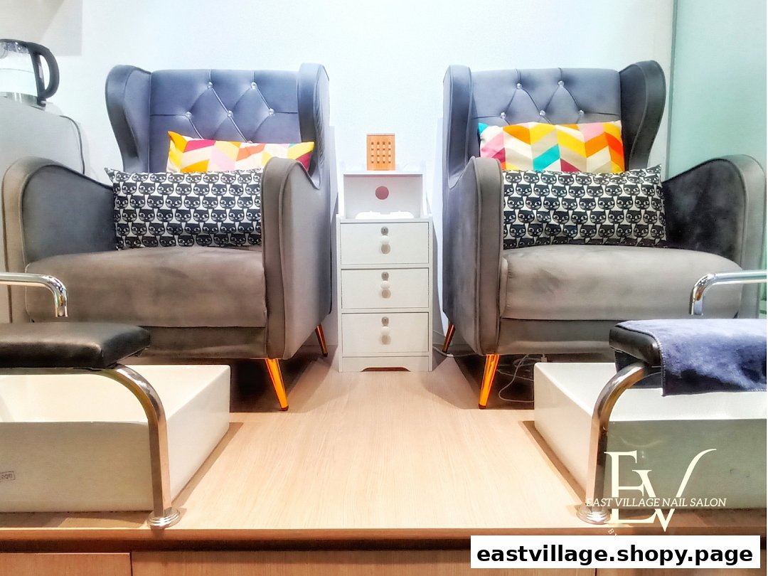 Two plush grey armchairs with colorful pillows and foot baths, set up for a relaxing nail salon experience.