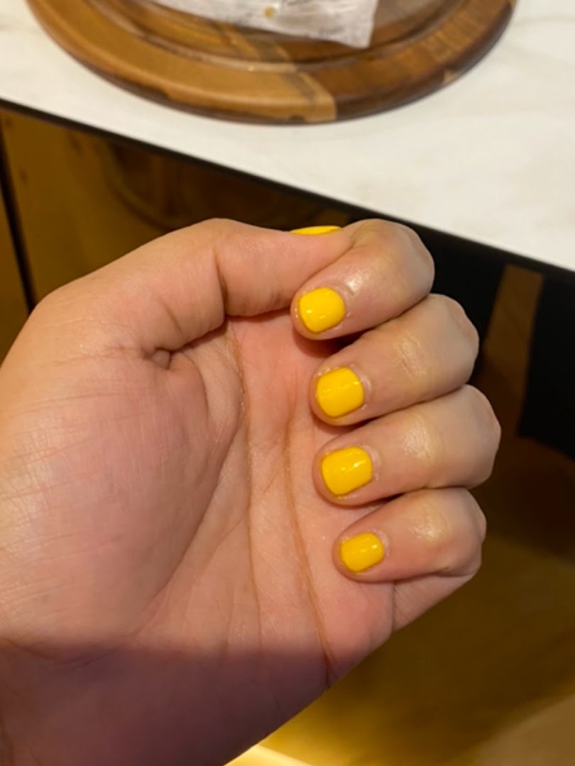 A hand showcasing freshly applied bright yellow nail polish, highlighting a vibrant manicure service.