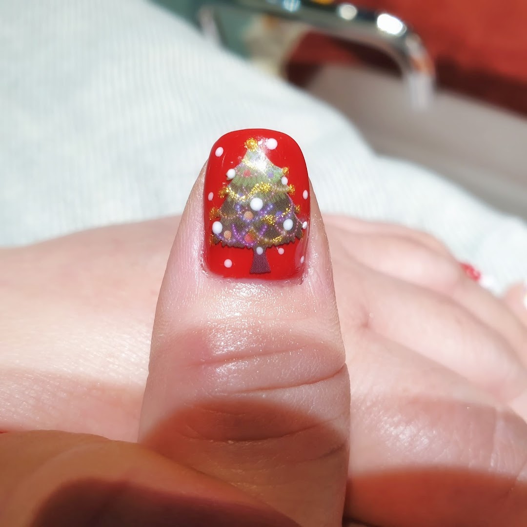 Close-up of a thumb featuring festive red nail polish with a detailed Christmas tree design.