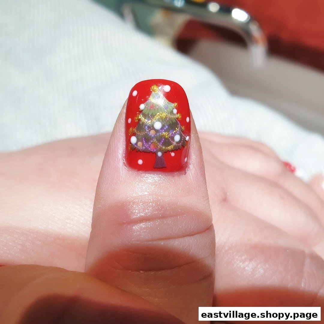 Close-up of a thumb featuring festive red nail polish with a detailed Christmas tree design.