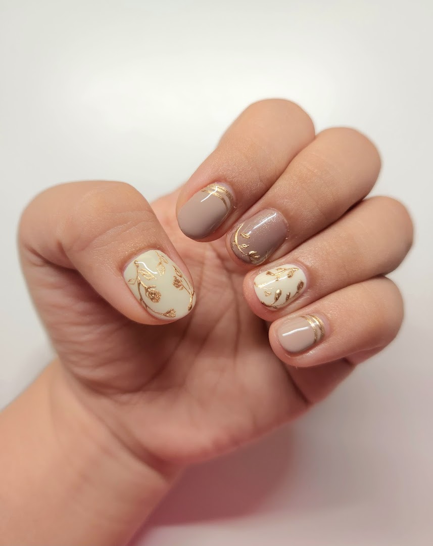 A hand showcasing elegant nail art with gold leaf and stripe designs on neutral polish.