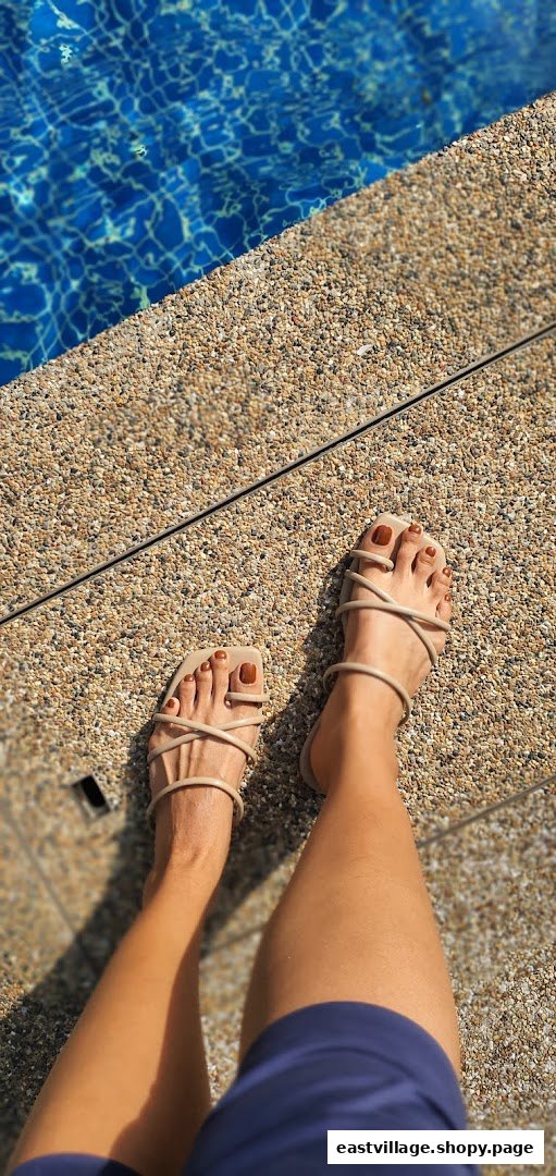 A person's feet with perfectly painted toenails and sandals by a sparkling blue swimming pool.