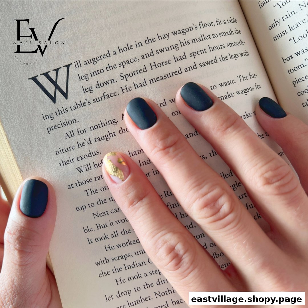 A hand with stylish dark matte nails and a gold foil accent nail holds an open book, featuring the salon's logo.