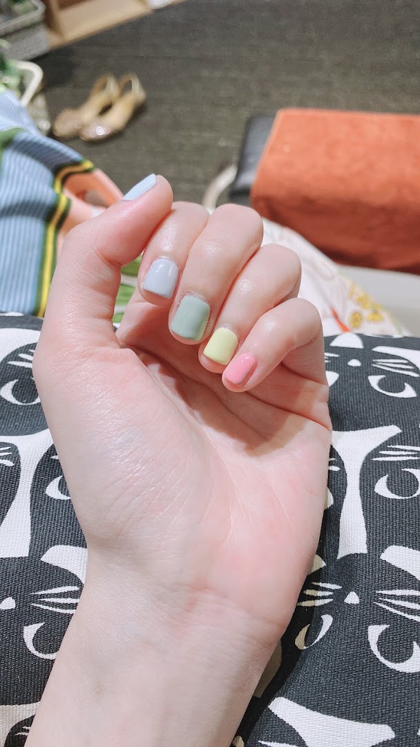 A close-up of a hand showcasing nails painted in various pastel colors, highlighting a fresh manicure.