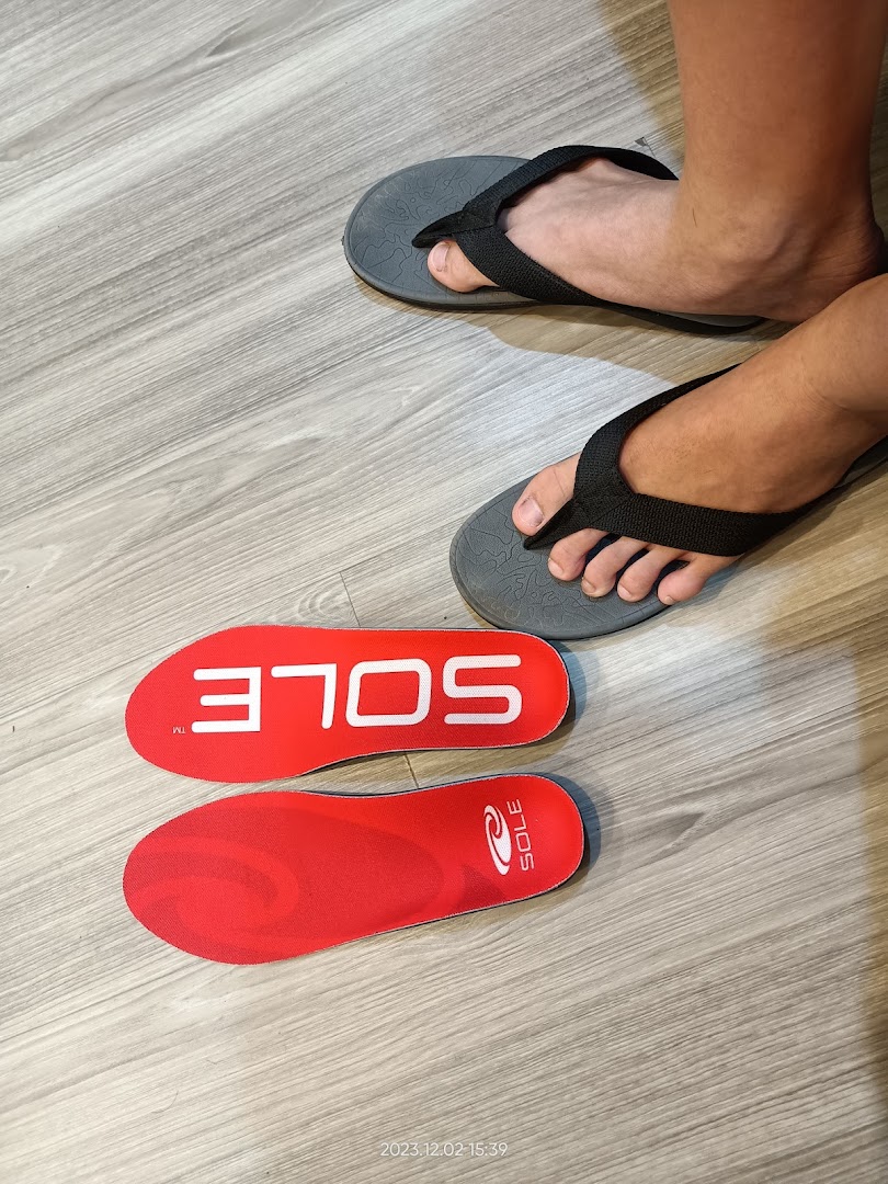 Feet in flip-flops next to two red insoles on a wooden floor, showcasing foot care products.