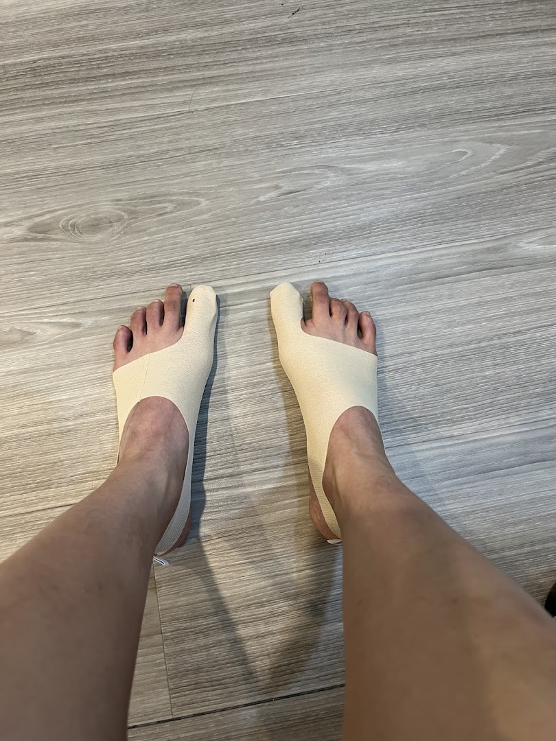 A person's feet wearing specialized toe alignment or bunion correction devices on a wooden floor.