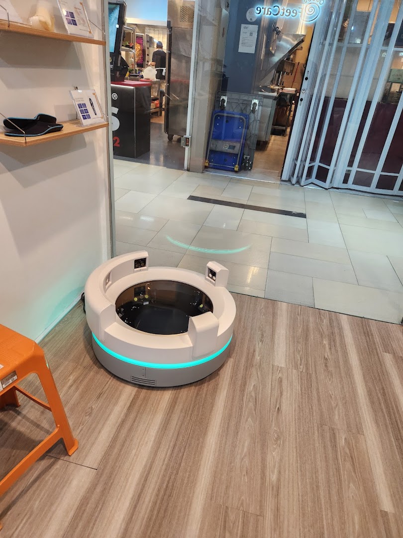 A modern circular foot scanning device with blue light, an orange stool, and product displays inside FeetCare East Village.