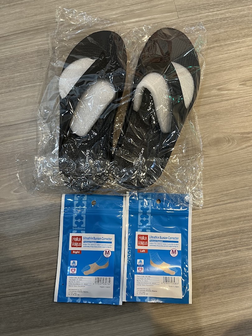Packaged black slippers and bunion corrector inserts displayed on a wooden floor.