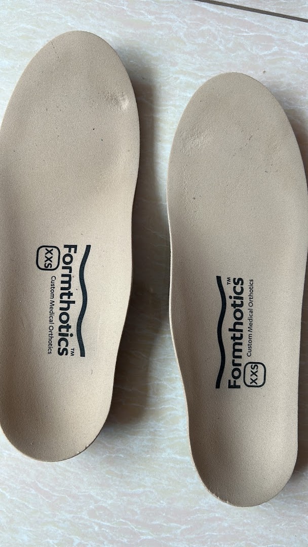 Two beige Formthotics custom medical orthotics insoles, size XXS, on a tiled surface.