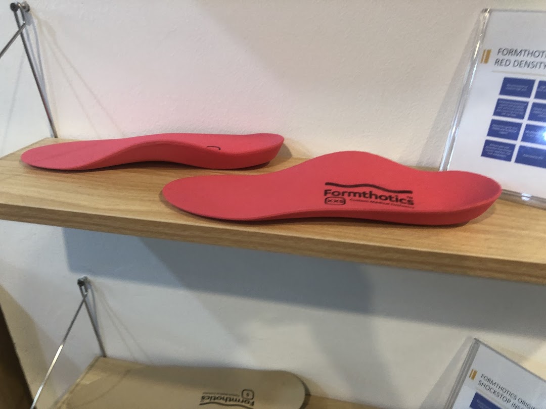 Two red Formthotics insoles displayed on a wooden shelf in a specialized foot care store.