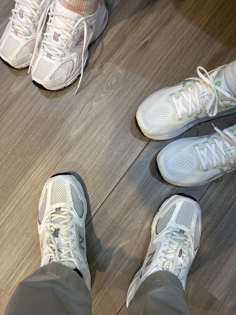Multiple pairs of feet wearing various white athletic shoes on a wooden floor, showcasing footwear options.