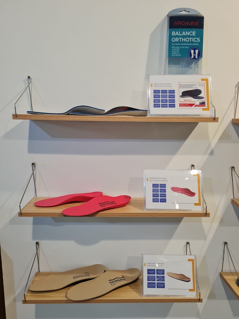 Various orthopedic insoles and foot care products are displayed on wooden shelves in a retail store.