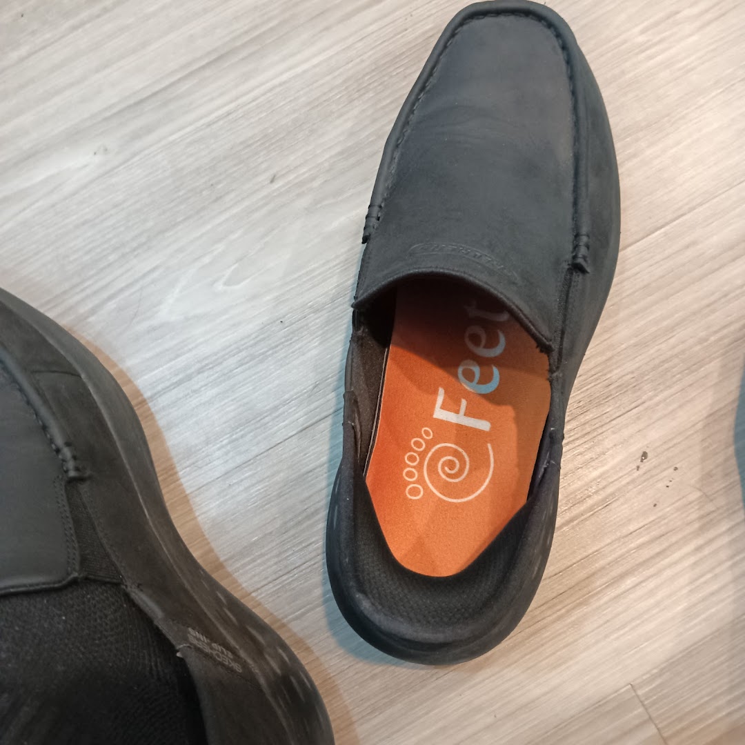 Close-up of a dark shoe on a wooden floor, revealing an orange insole with 'Feet' branding.