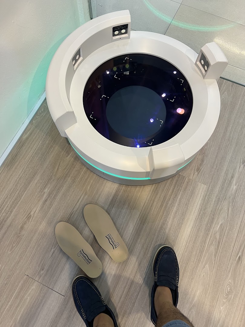 A person's feet and insoles next to a foot scanning machine on a wooden floor.