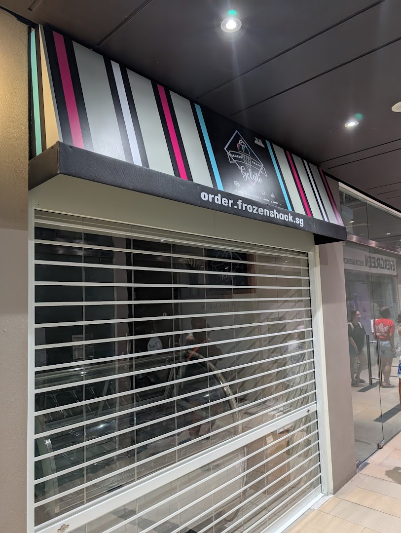 The closed storefront of Frozen Shack, featuring a colorful striped awning and a security shutter.