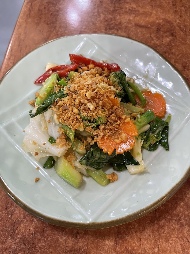 A vibrant plate of stir-fried vegetables topped with crispy garlic, served on a light green leaf-shaped plate.