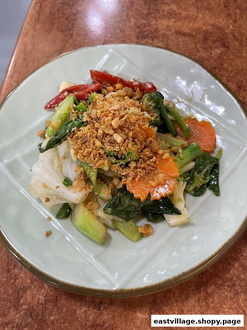 A vibrant plate of stir-fried vegetables topped with crispy garlic, served on a light green leaf-shaped plate.